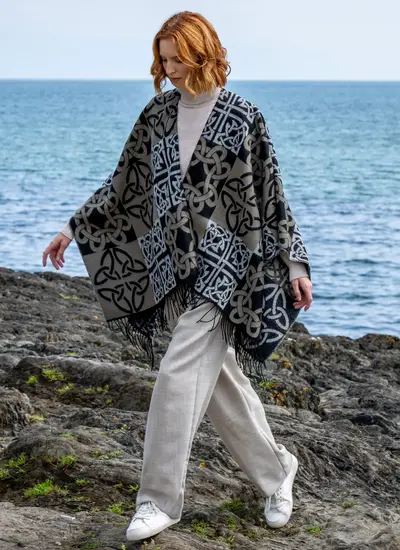Red head model walking along stony beach in a black and tan celtic knot shawl